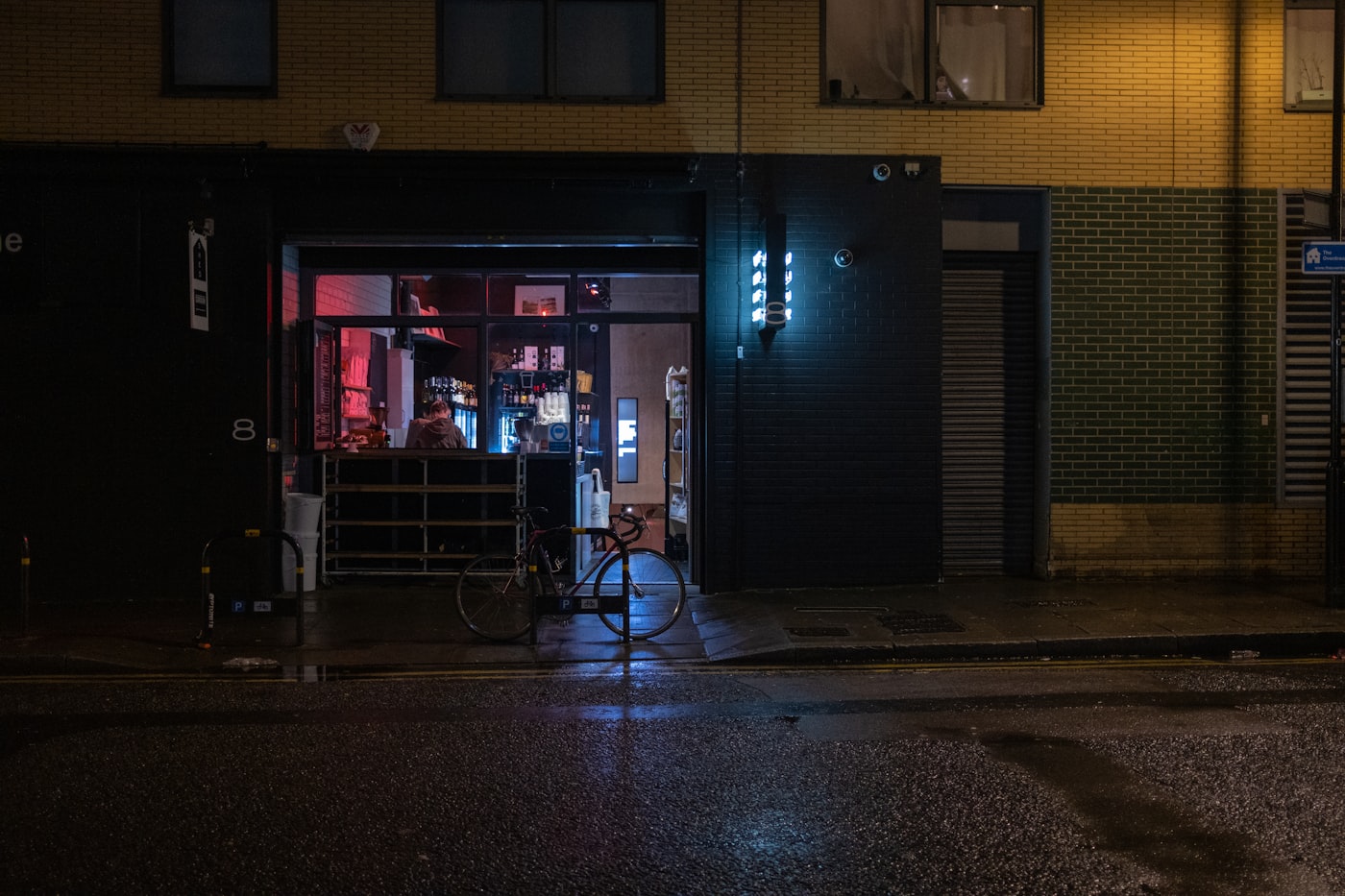 A small London café at night seen from the street, lit from inside, with a bicycle parked outside